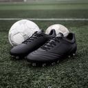Zwarte voetbalschoenen met noppen naast een voetbal op kunstgras