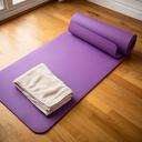 Lila yogamat op een houten vloer met een opgevouwen handdoek