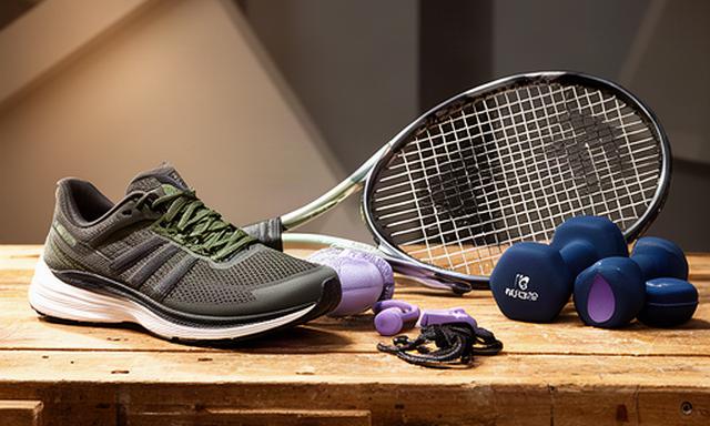 Sportattributen zoals een tennisracket, hardloopschoenen en fitnessgewichten op een houten werkbank